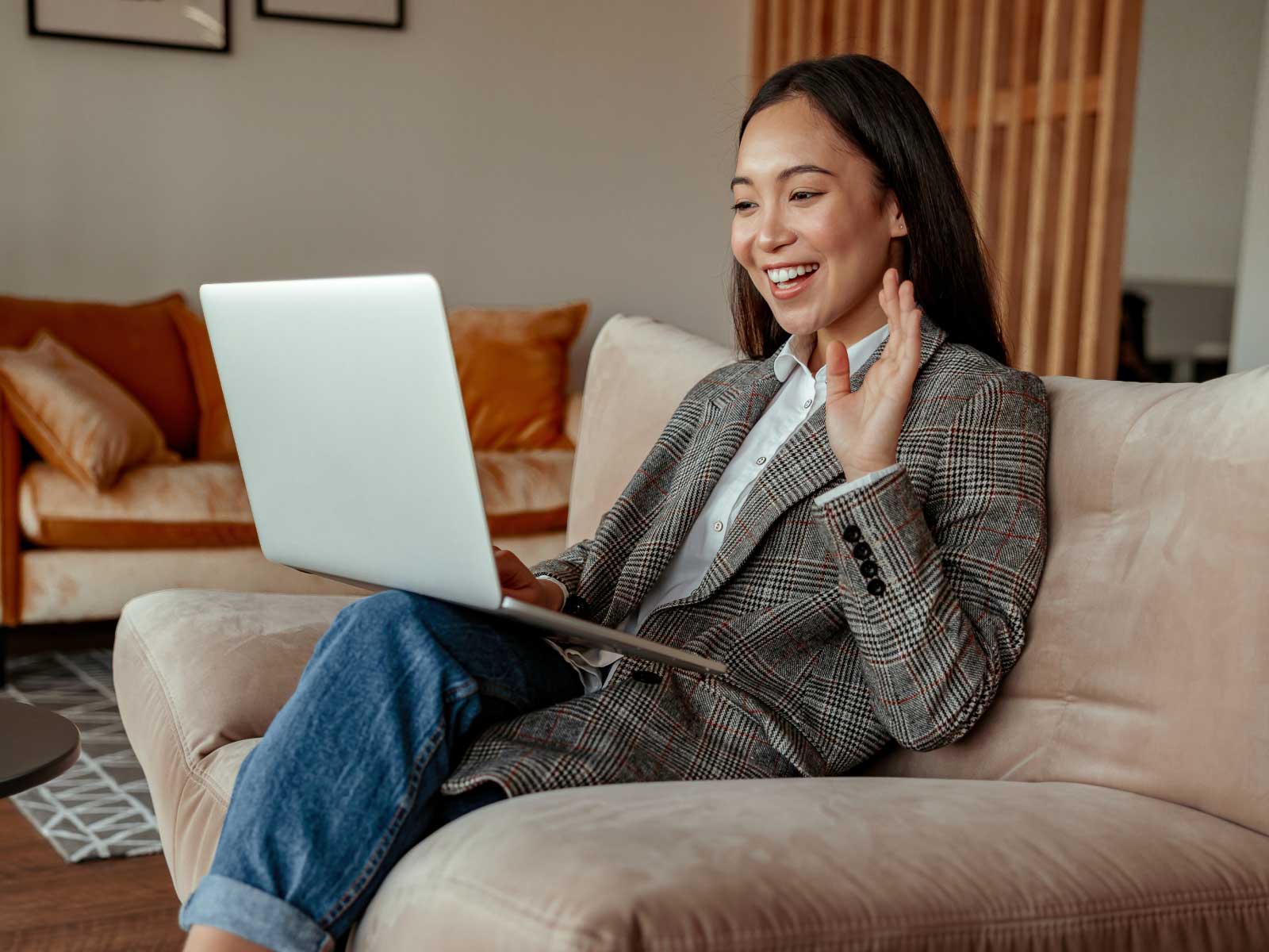 Woman on couch waving at laptop